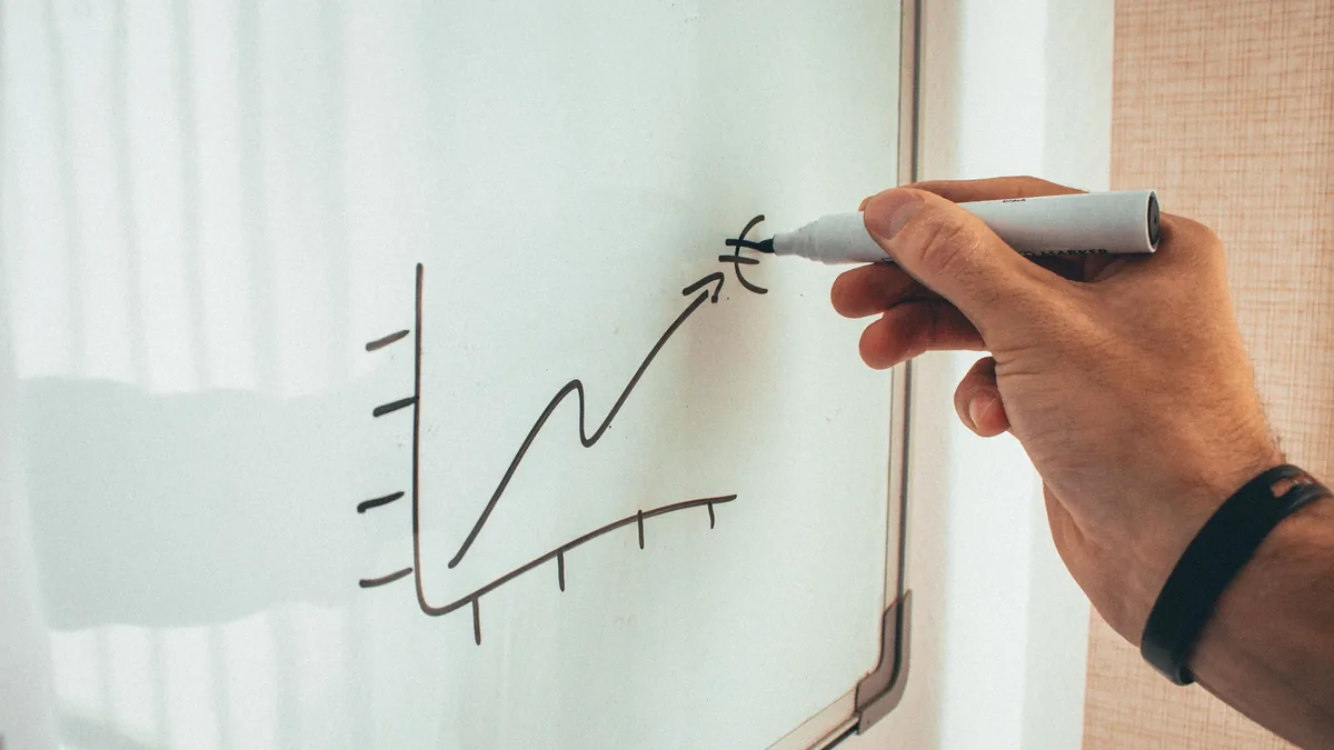 A hand drawing an upward-trending growth chart on a whiteboard